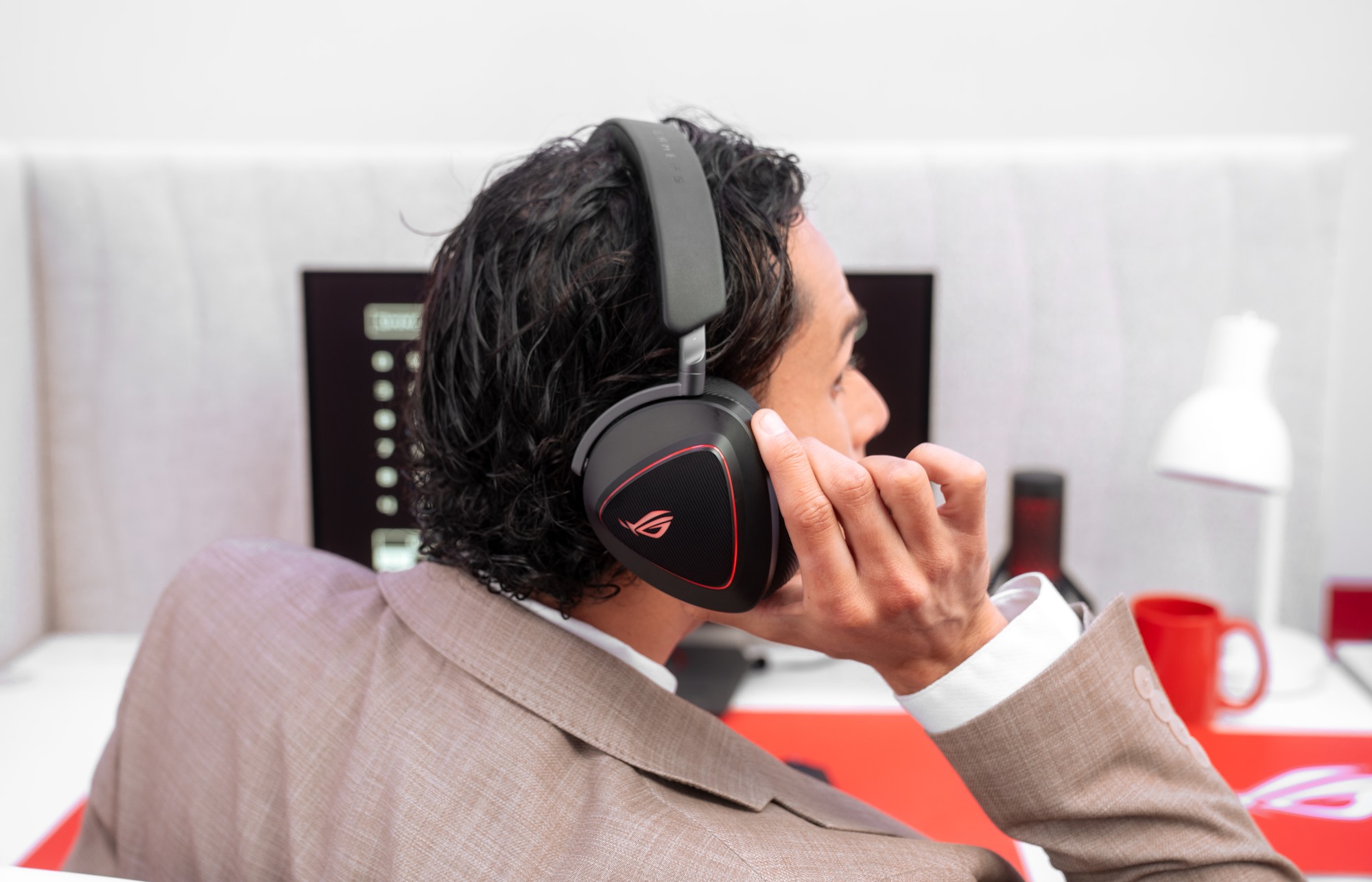 A young man in a suit turns to hear someone talking to him, lifting the cup of his ROG Delta II headset so that he can listen